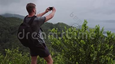 一个背着背包的旅行者，<strong>站在山顶</strong>，在他的手机上拍摄一幅风景。